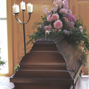 Holzsarg mit Blumenschmuck und Kerzenständern in einer Trauerhalle bei einer Beerdigung.