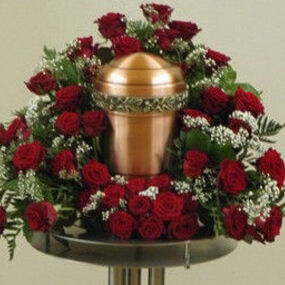 Kupferfarbene Urne mit rotem Rosenkranz und weißen Blumen für Beerdigung oder Trauerfeier.