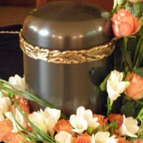 Eine Urne mit goldener Verzierung ist von weißen und orangefarbenen Blumen umgeben.